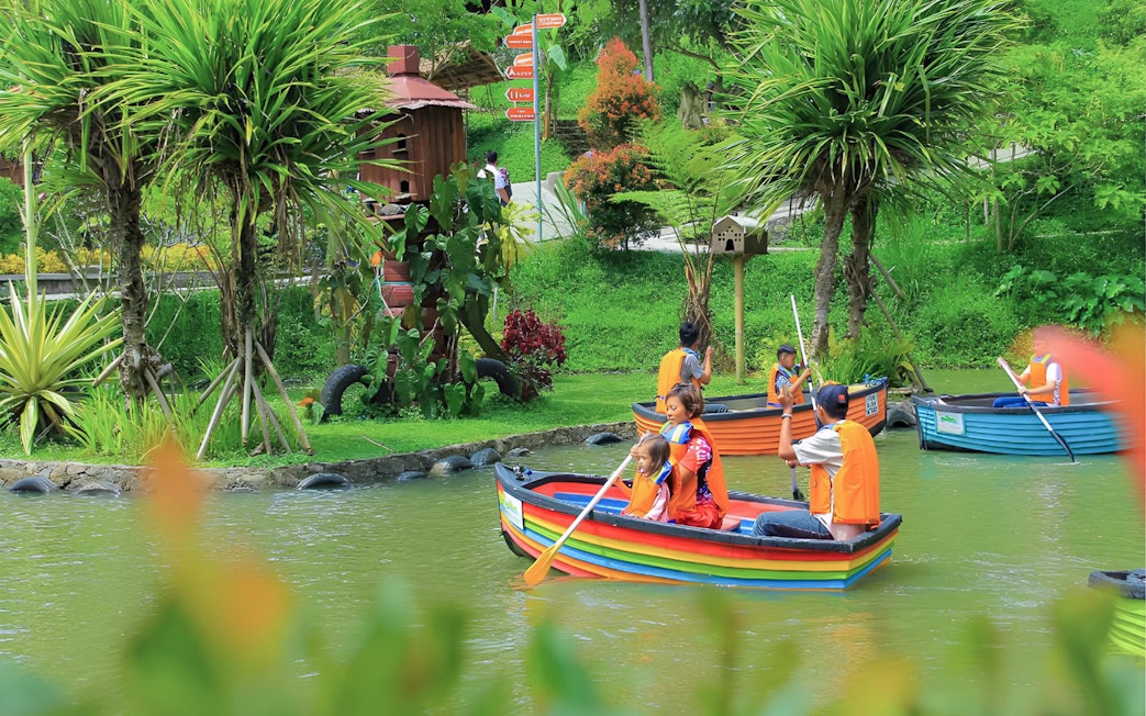 Visitors paddling colorful boats at Dago Dreampark, Bandung, surrounded by lush greenery.