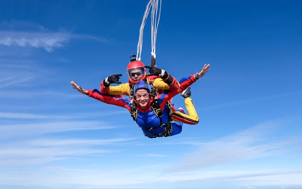 Tandem skydivers freefalling over Abu Dhabi with clear blue sky.