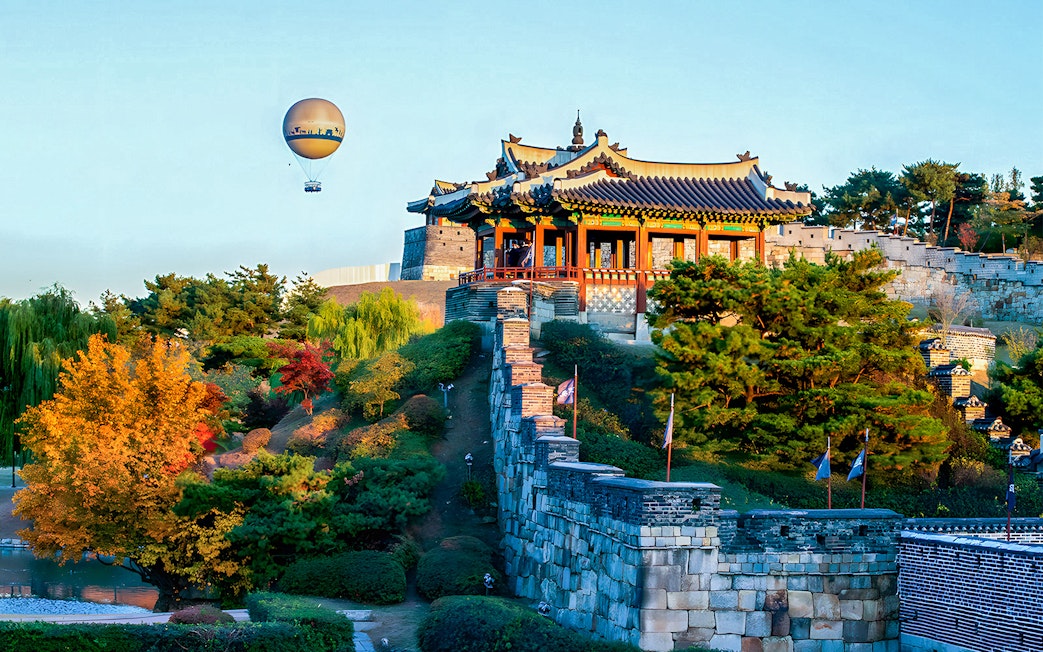 Hot air balloon over Suwon Hwaseong Fortress with autumn trees, part of Korean Folk Village tour.