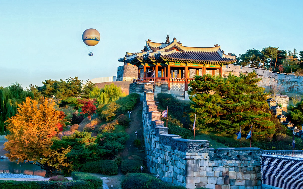 Hot air balloon over Suwon Hwaseong Fortress with autumn trees, part of Korean Folk Village tour.