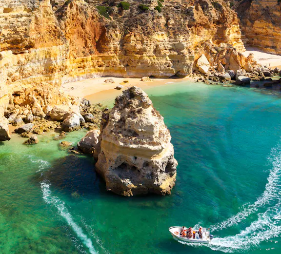 Tourists on boats exploring coastal caves near a sandy beach in Algarve, Portugal.