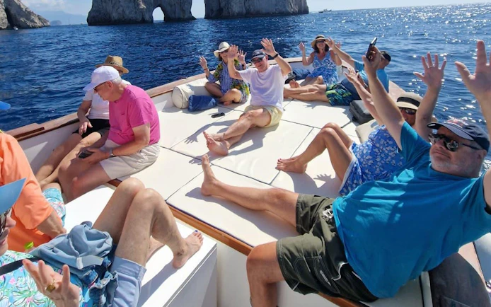 Tourists relaxing on a boat near Capri's Faraglioni rocks during a swimming stop.