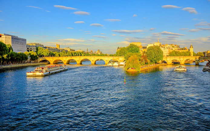 Seine River cruise boats passing under Pont Neuf in Paris.