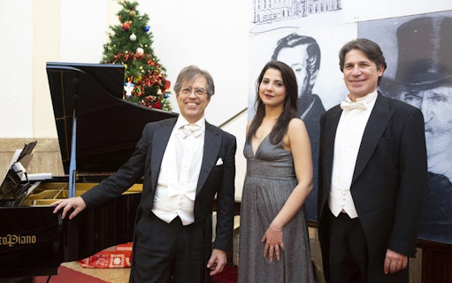 Opera performers in formal attire beside a grand piano with a Christmas tree in the background.