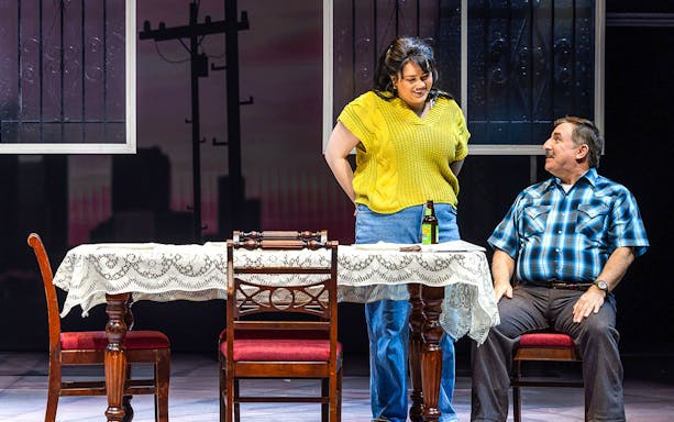 Scene from Real Women Have Curves: The Musical with two actors at a table.