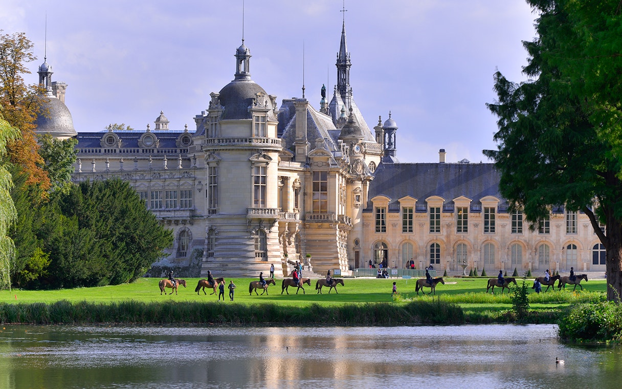 Chateau of Chantilly with visitors on horseback by the lake, France.
