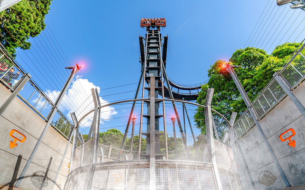 Oblivion ride drop tower at Alton Towers with blue sky and trees in background.
