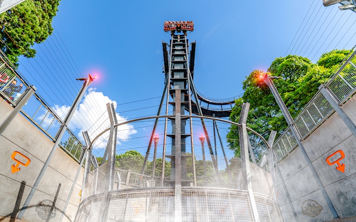 Oblivion ride drop tower at Alton Towers with blue sky and trees in background.