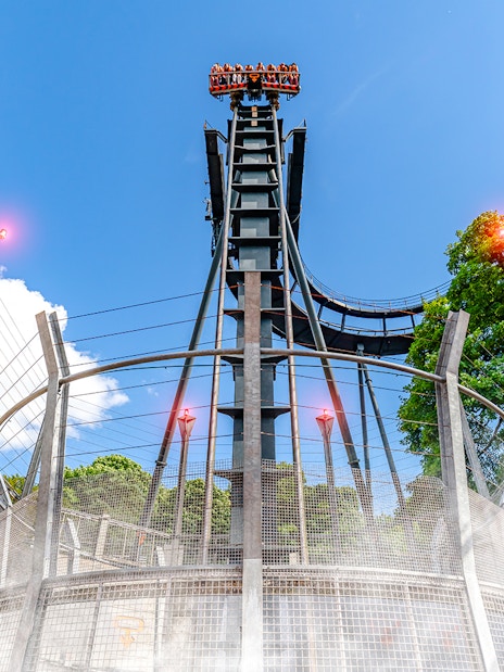 Oblivion ride drop tower at Alton Towers with blue sky and trees in background.