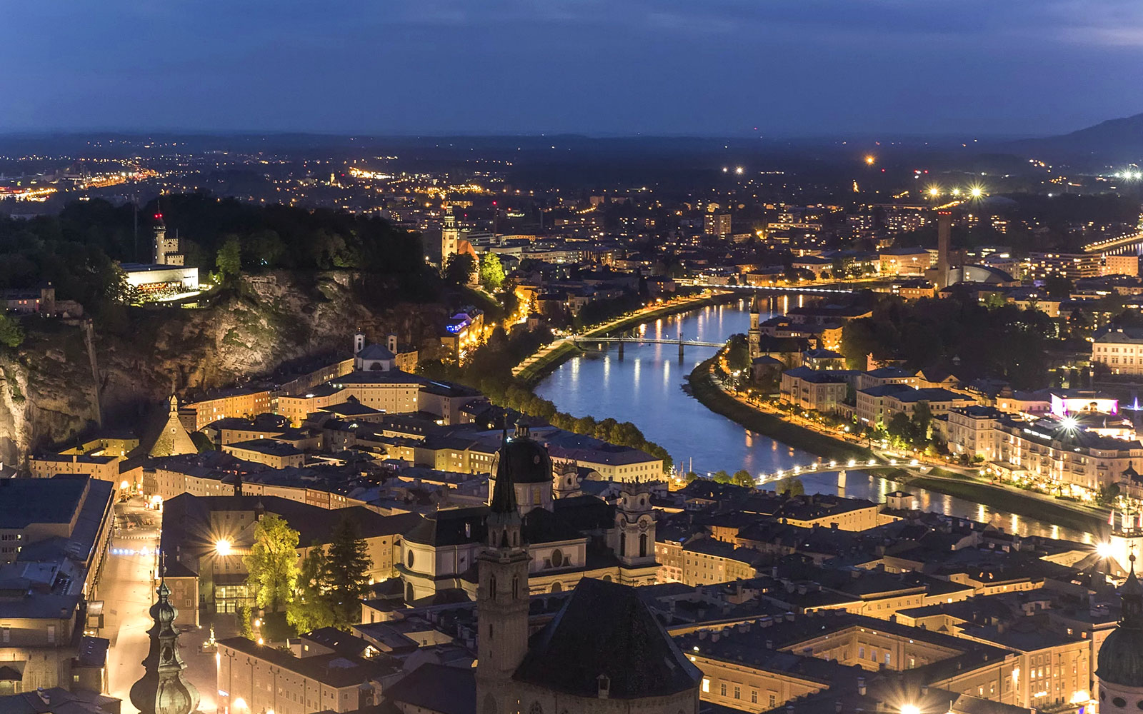 Fortress Hohensalzburg overlooking Salzburg at night with illuminated cityscape and river.