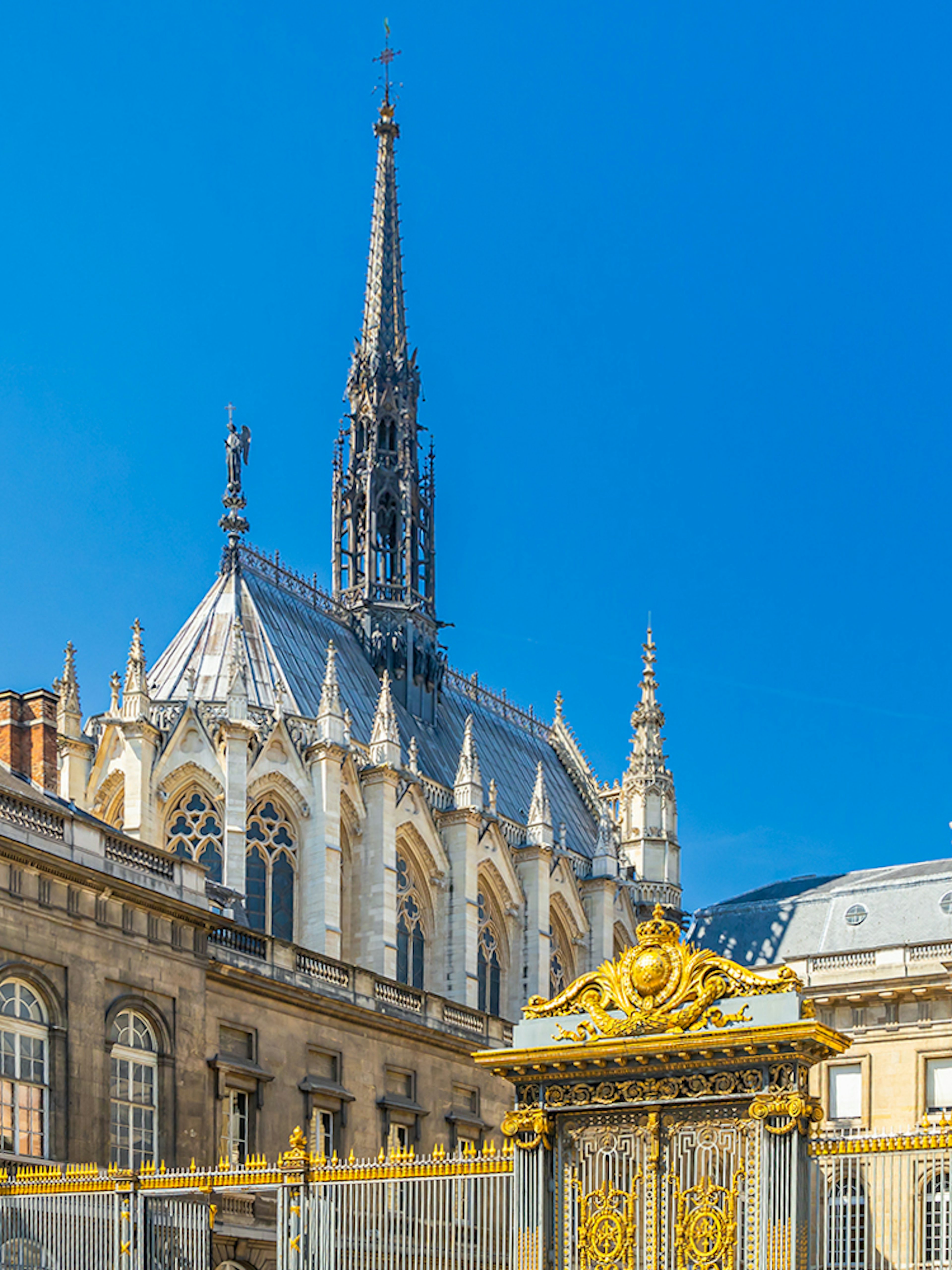 Sainte Chapelle spire and Conciergerie facade in Paris with ornate golden gate.