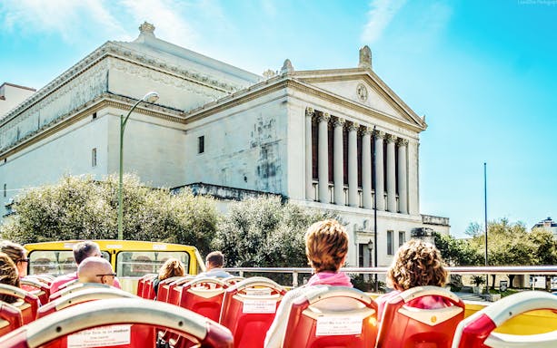 Open-top bus passing a historic building in San Antonio during a hop-on-hop-off tour.