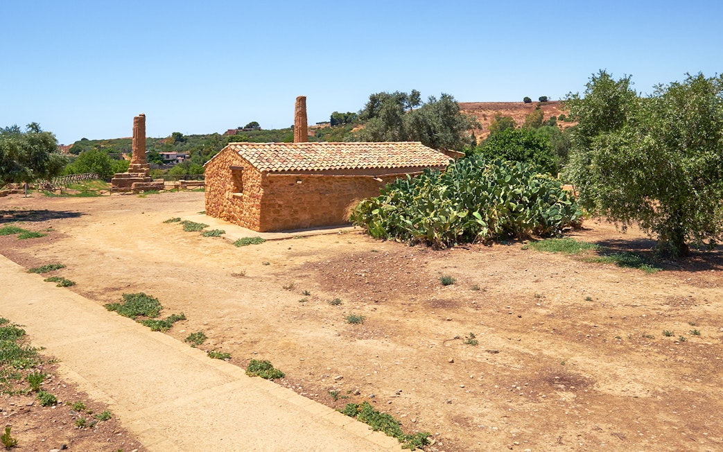 Stone building and ancient ruins in Valley of the Temples, Sicily, surrounded by greenery.