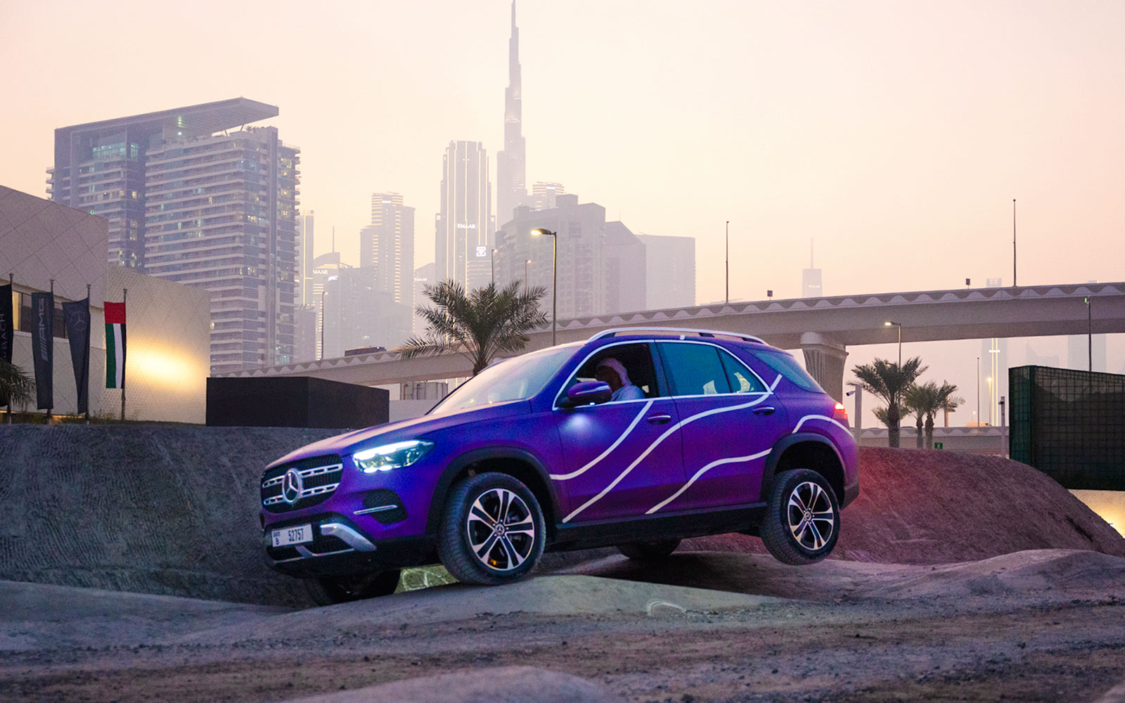 Mercedes-Benz SUV on off-road track with Dubai skyline in background.