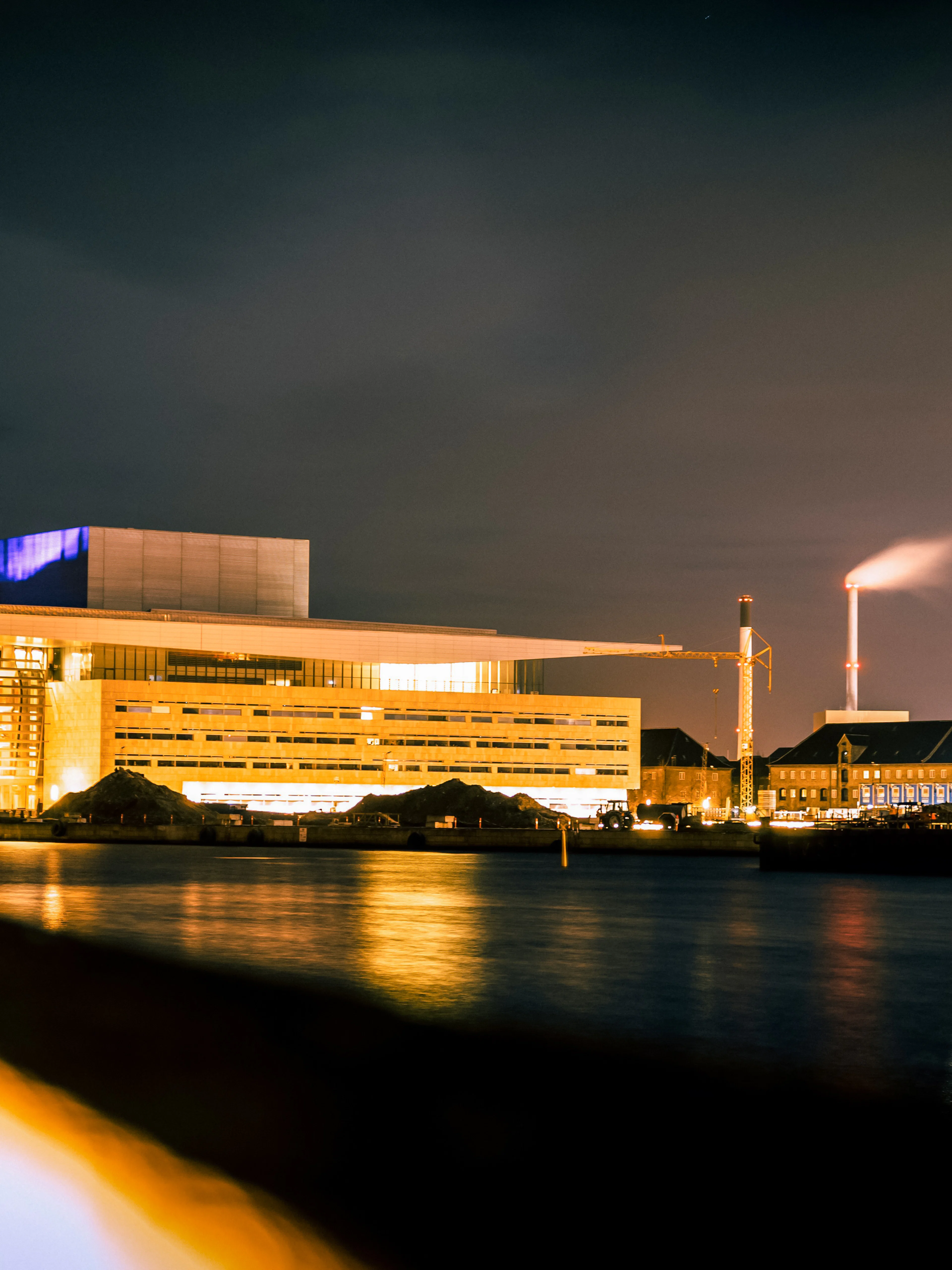 Copenhagen Opera House illuminated at night, viewed from across the water.