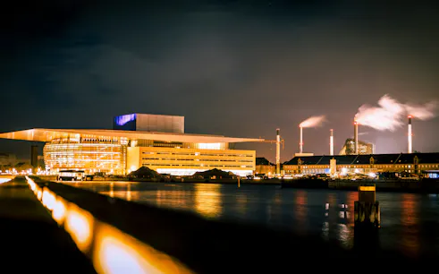 Copenhagen Opera House illuminated at night, viewed from across the water.