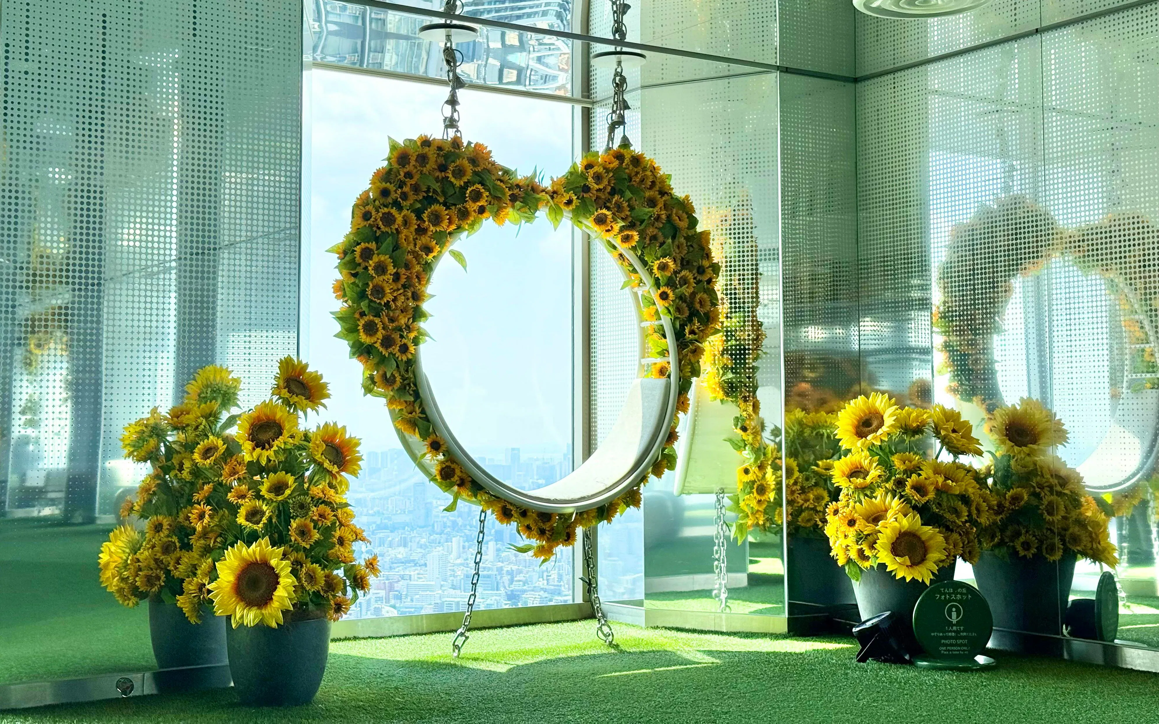 Sunflower-decorated swing at Sunshine 60 Observatory Tenbou Park with city view.