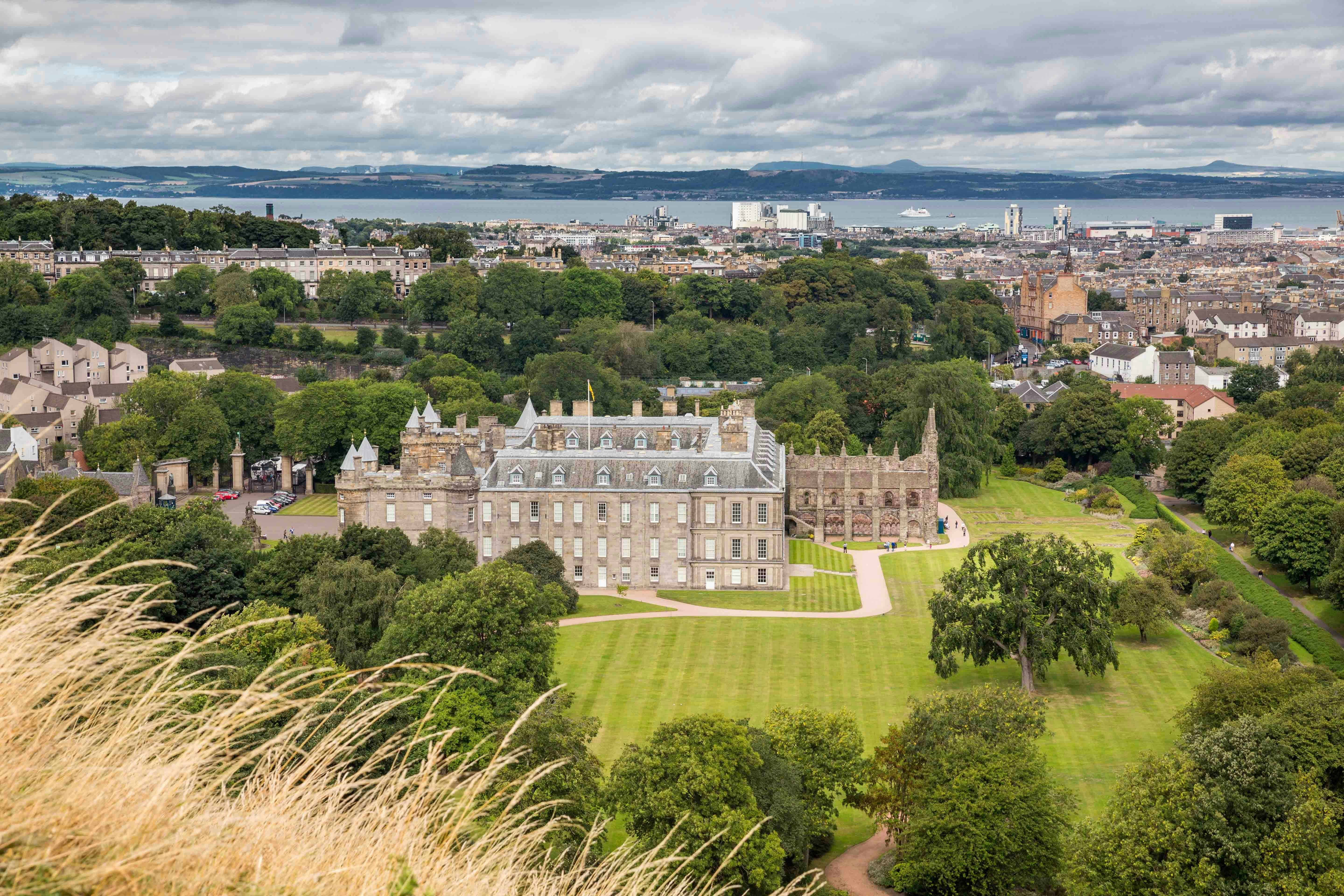 Palace of Holyroodhouse with gardens and Edinburgh cityscape in the background.