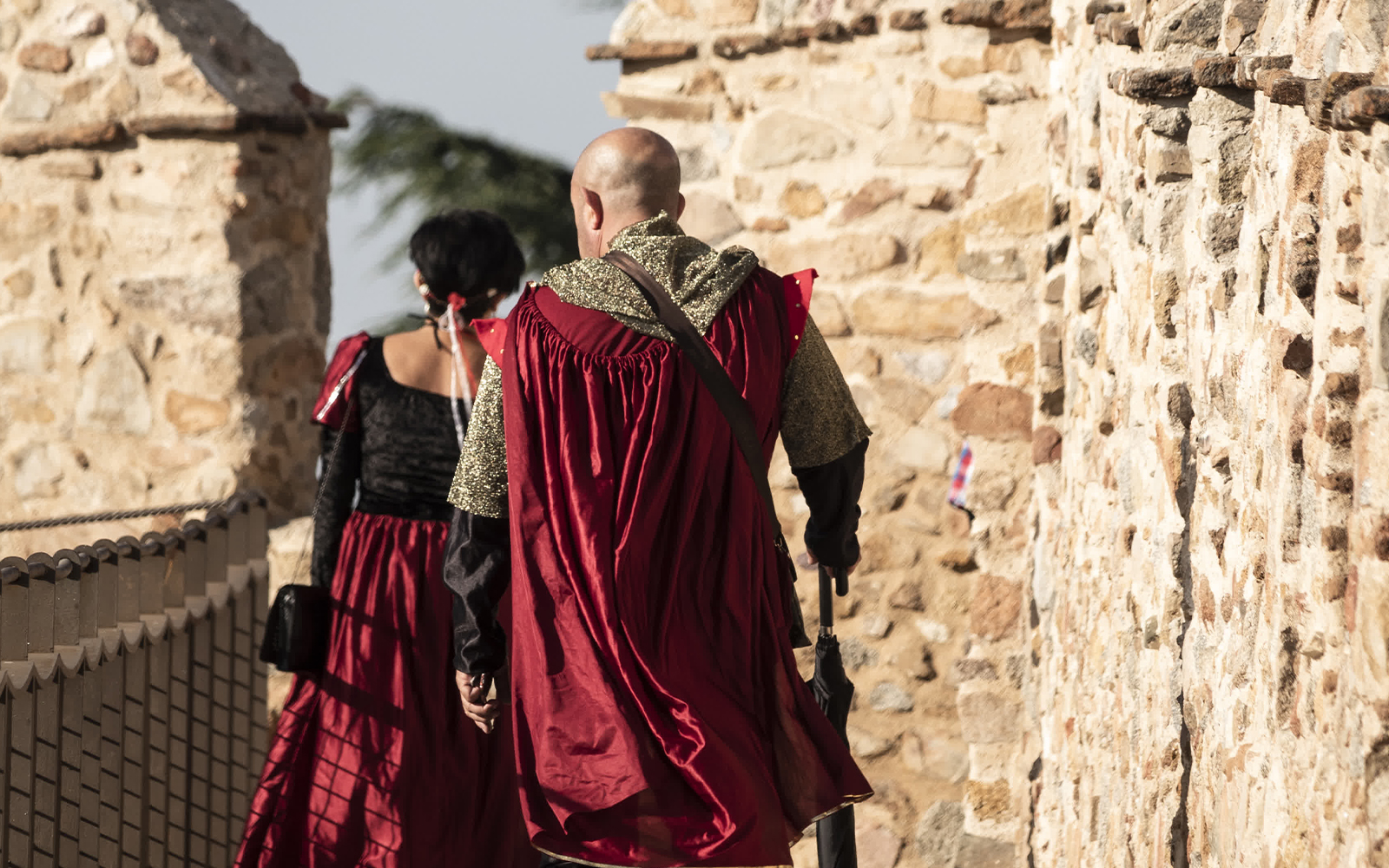 Medieval fair attendees in period costumes walking along Avila's ancient stone walls.