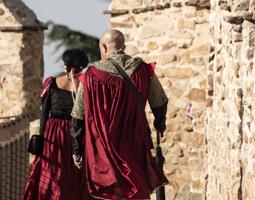 Medieval fair attendees in period costumes walking along Avila's ancient stone walls.