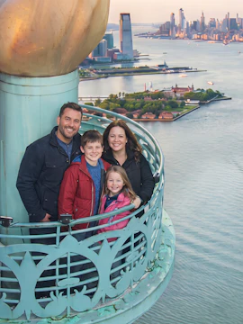 Family on the Statue of Liberty torch balcony with NYC skyline in the background.