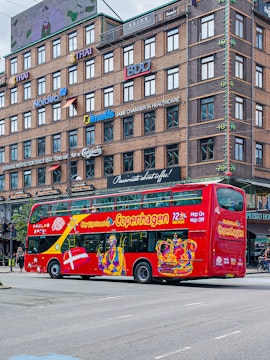 Red double-decker bus for city sightseeing in Copenhagen, Denmark, near a brick building.