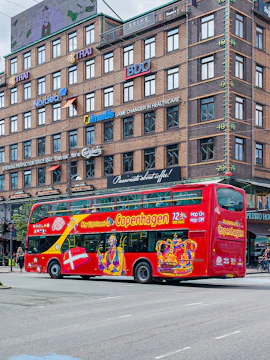 Red double-decker bus for city sightseeing in Copenhagen, Denmark, near a brick building.
