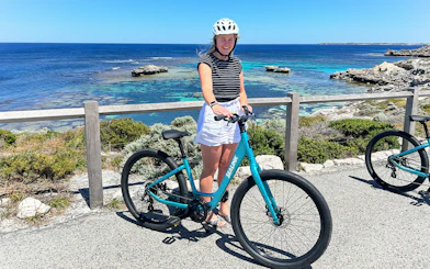 Person with a bike on Rottnest Island overlooking the ocean during a guided bus tour.