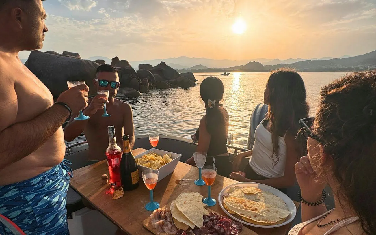 Group enjoying aperitif on dinghy at sunset near Arbatax, Nuoro.