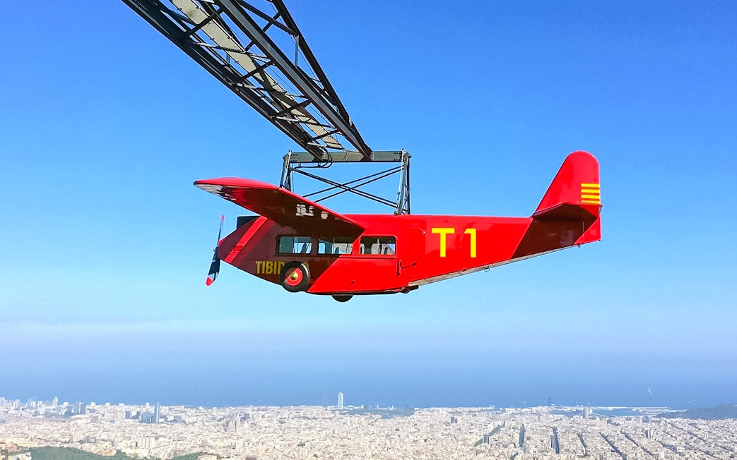 Red airplane ride at Tibidabo Amusement Park with Barcelona cityscape below.