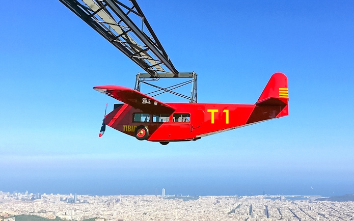 Red airplane ride at Tibidabo Amusement Park with Barcelona cityscape below.