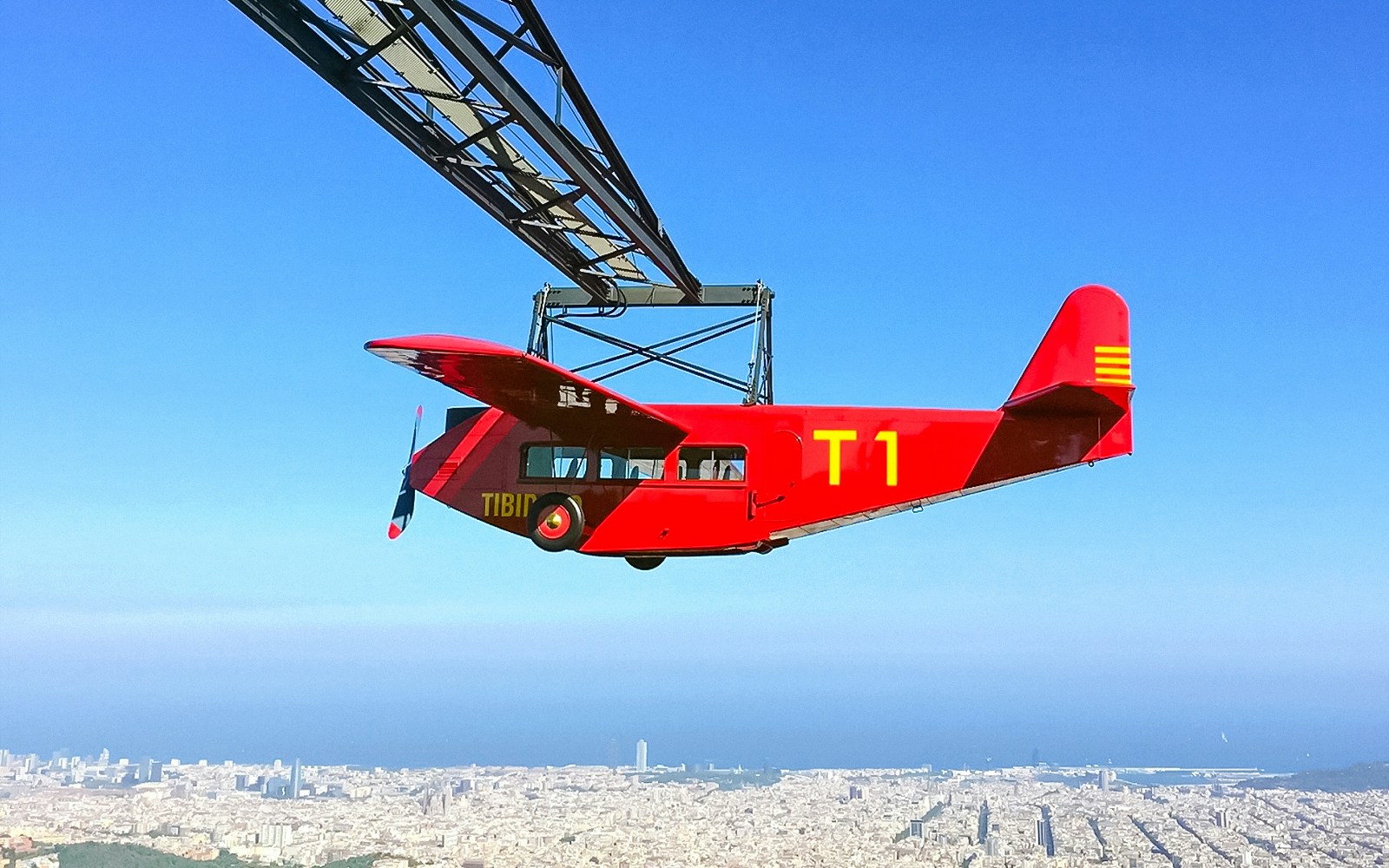 Red airplane ride at Tibidabo Amusement Park with Barcelona cityscape below.