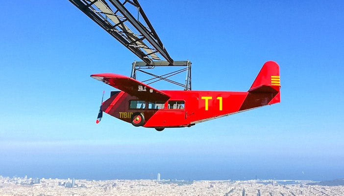 Red airplane ride at Tibidabo Amusement Park with Barcelona cityscape below.
