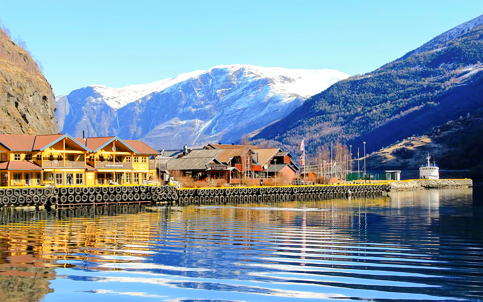 Waterfront buildings in the village of Flåm, Western Norway, with snow-capped mountains in the background.