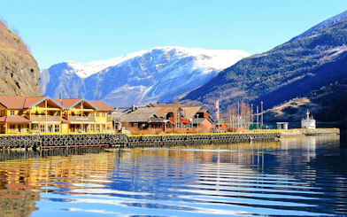 Waterfront buildings in the village of Flåm, Western Norway, with snow-capped mountains in the background.
