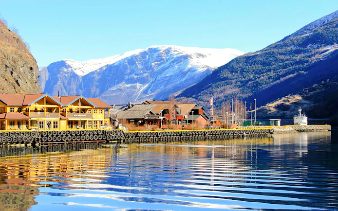 Waterfront buildings in the village of Flåm, Western Norway, with snow-capped mountains in the background.