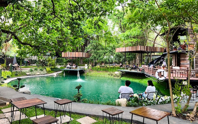 People relaxing by a lush jungle pond at Chom Cafe, Chiang Mai, Thailand.