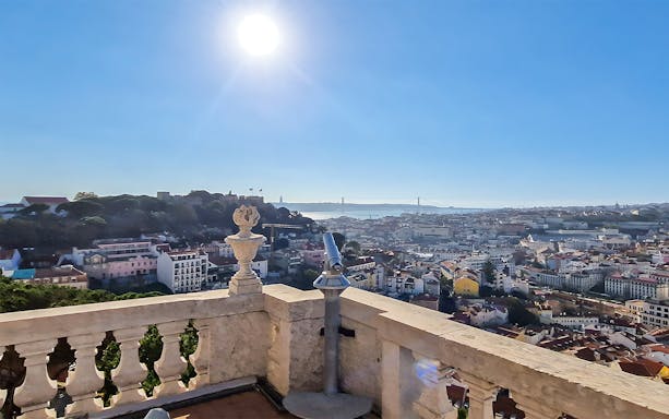 Telescope overlooking Lisbon from Church of Graca viewpoint with cityscape and bridge.