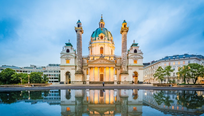 Karlskirche in Vienna with illuminated facade reflecting in a pond.
