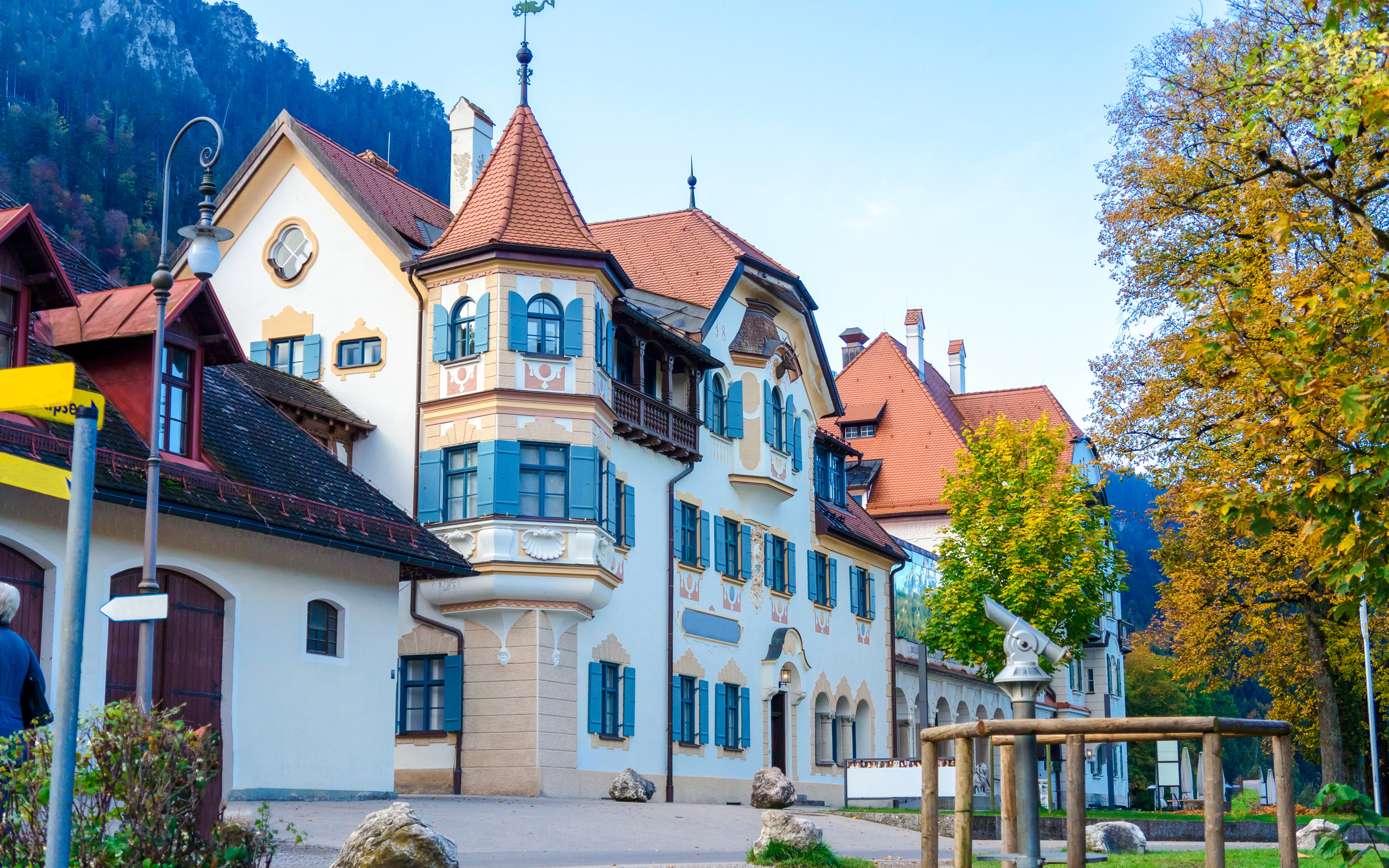 Historic building with blue shutters in Schwangau Village, Germany, surrounded by autumn trees.