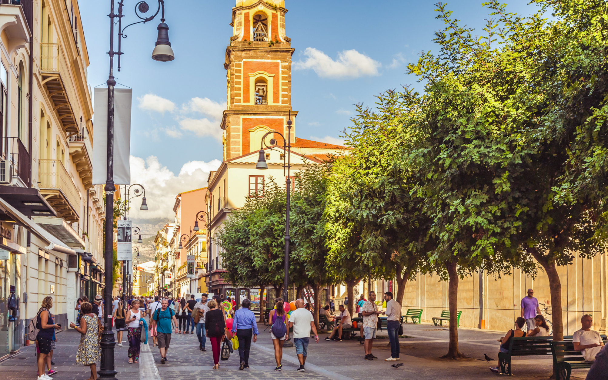 Crowded Corso Italia street in Sorrento with people walking and a bell tower in view.