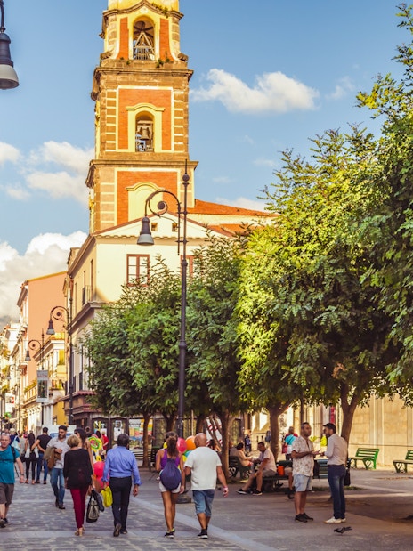 Crowded Corso Italia street in Sorrento with people walking and a bell tower in view.