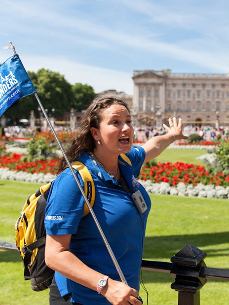 Tour guide leading a group near Buckingham Palace gardens in London.
