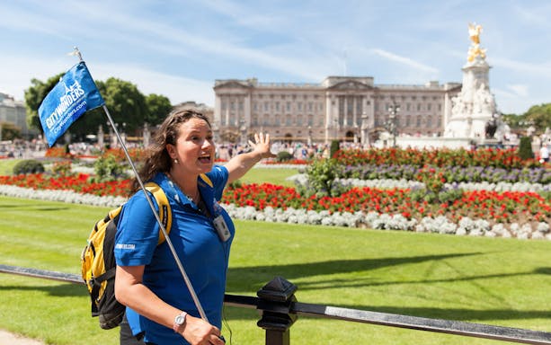 Tour guide leading a group near Buckingham Palace gardens in London.