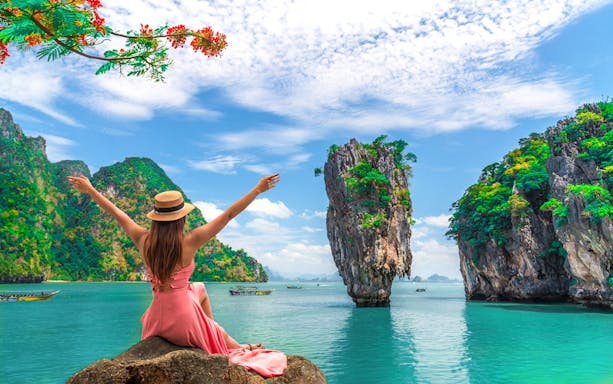 Woman enjoying view of Phang Bay Islands from rock, with limestone cliffs and turquoise water, Phuket tour.