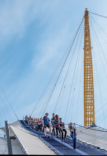 Visitors climbing the O2 Arena roof in London with safety gear.