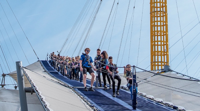 Visitors climbing the O2 Arena roof in London with safety gear.
