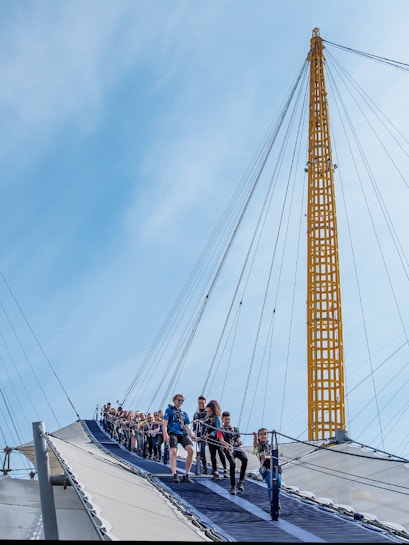 Visitors climbing the O2 Arena roof in London with safety gear.