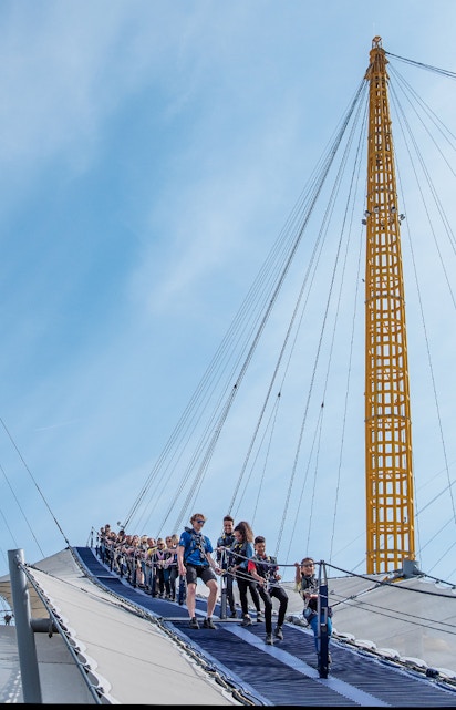 Visitors climbing the O2 Arena roof in London with safety gear.
