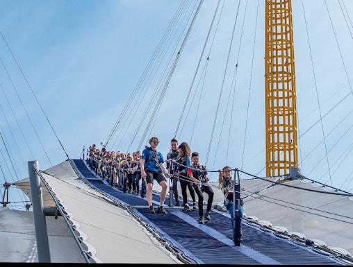 Visitors climbing the O2 Arena roof in London with safety gear.